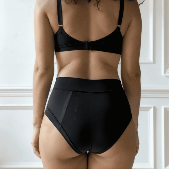 Detail of woman in her 30s with her back to the viewer wearing the high-waisted Emanate brief in Obsidian black made from OEKO TEX certified fabric