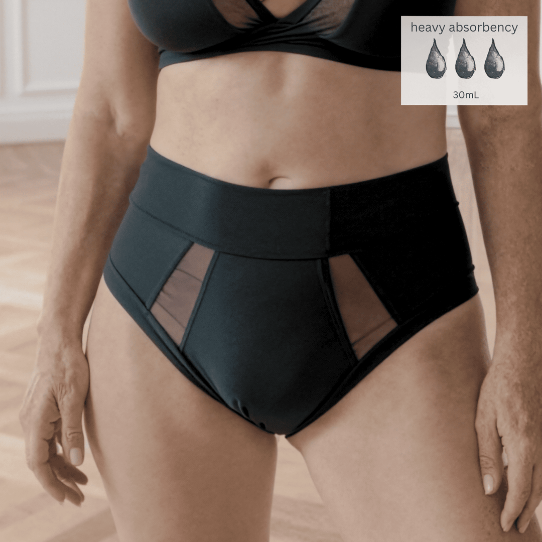 Detail of a woman in her 40s wearing the size Medium high-waisted Emanate brief in Obsidian black made from OEKO TEX certified fabric. There is a Heavy Absorbency icon in the top right of the image indicating they absorb 30mL of liquid