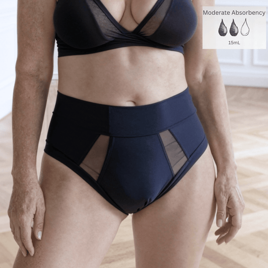 Detail of woman in her 40s wearing the high-waisted Emanate brief in Slate Navy. There is a Moderate Absorbency icon in the top right of the image