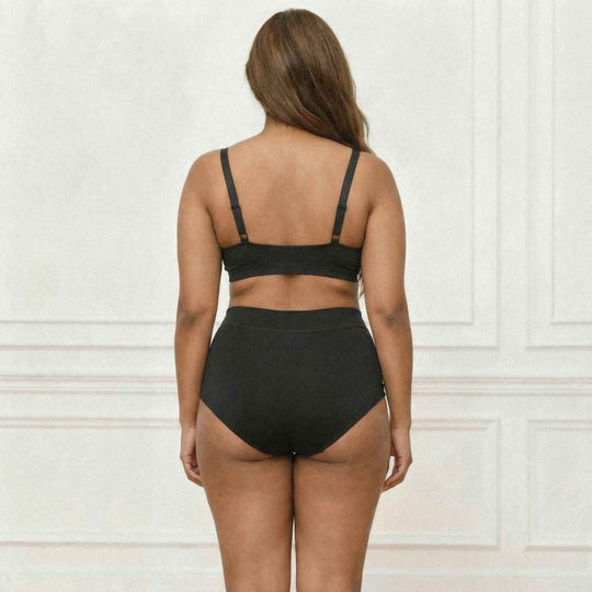 Woman standing with her back to the viewer wearing the Wicks Intimates high waisted brief in black.