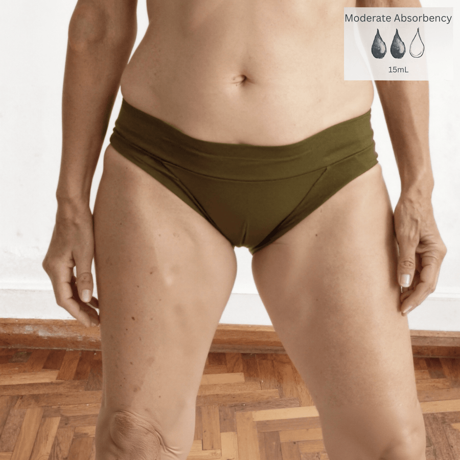Detail of woman in her 60s facing forward wearing a size Medium Engineered brief in Moss green made from GOTS certified organic cotton. There is a moderate absorbency icon in the top right of the image