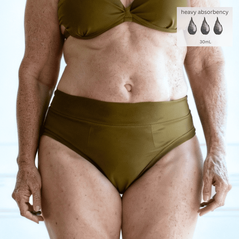 Detail of woman in her 70s wearing the High Waisted Basic brief in Moss green made from GOTS certified organic cotton. The Heavy Absorbency icon is in the top right of the image indicating this garment can absorb up to 30mL of liquid