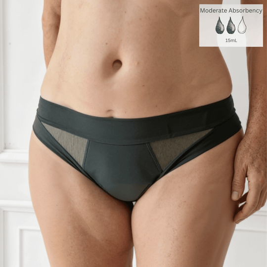Detail of woman in her 50s facing forward wearing the low-rise Swept Away brief in Forest green made from OEKO TEX certified fabric. Moderate Absorbency icon in the top right of the image