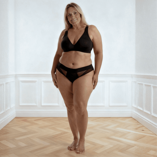 Woman in her 50s facing the viewer wearing the low-rise Swept Away brief in Obsidian Black made from OEKO TEX certified fabric